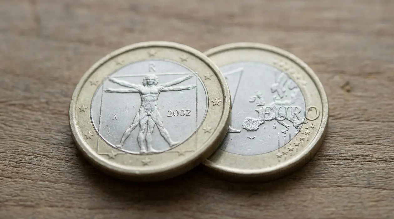 Due monete da 1 euro su un tavolo di legno, una con l’anno 2002 e il disegno dell’Uomo Vitruviano