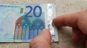 Dettaglio di una banconota da 20 euro con una mano che indica la striscia olografica di sicurezza