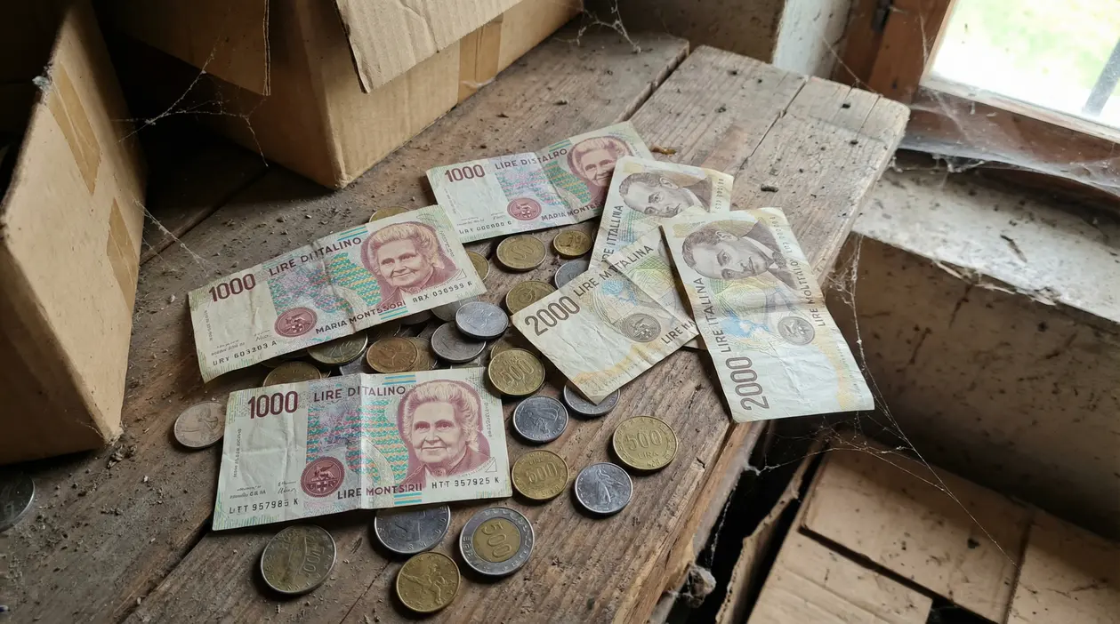 Vecchie banconote e monete in lire italiane appoggiate su un tavolo impolverato in soffitta