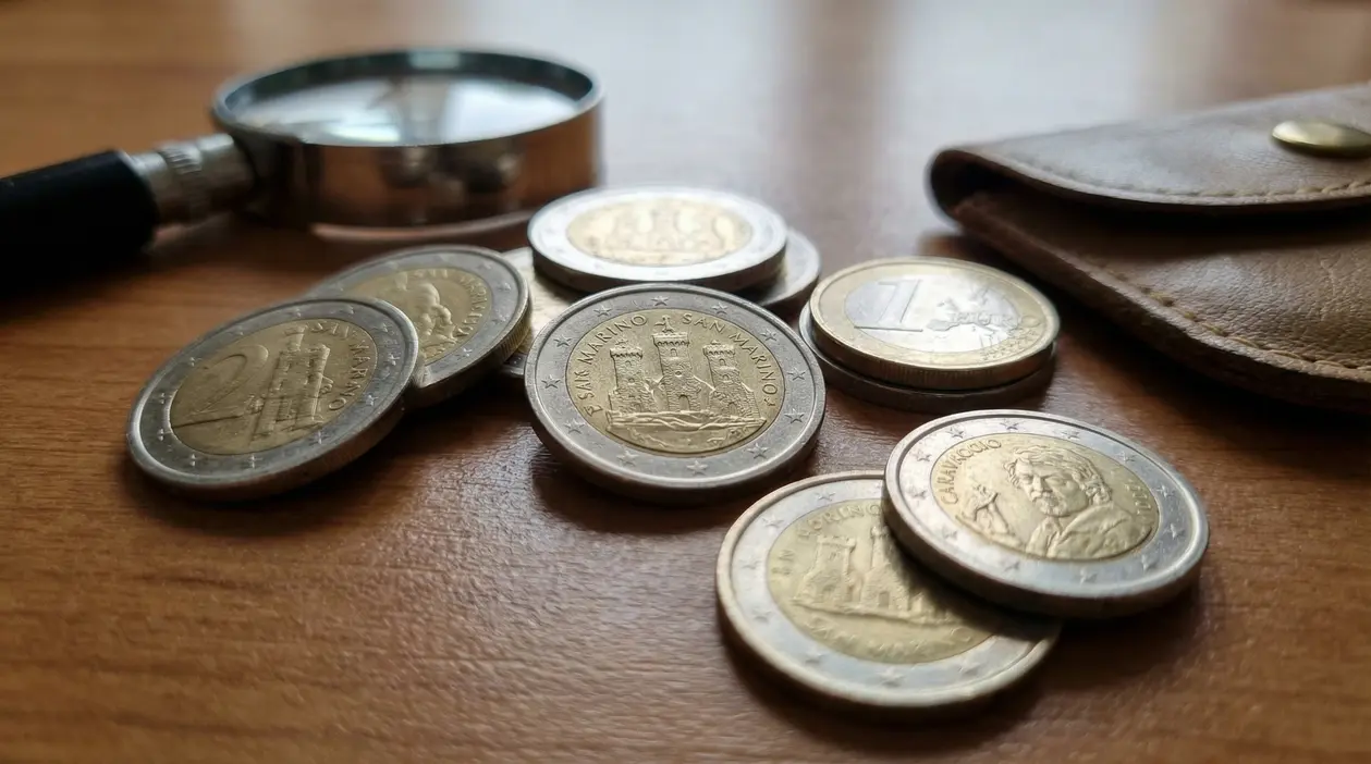 Monete euro di San Marino sparse su un tavolo accanto a una lente d'ingrandimento e un portafoglio