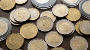 Monete in euro di diversi Paesi europei, incluse emissioni di Monaco e Vaticano, su un tavolo in legno