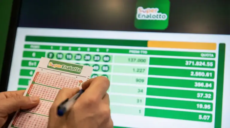 Mani che compilano una schedina del SuperEnalotto davanti a uno schermo con numeri e quote della vincita