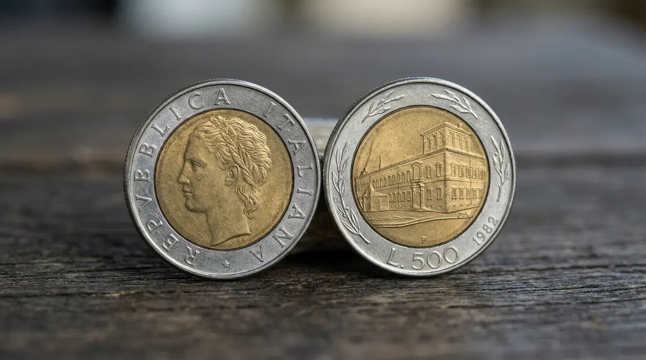 Due monete da 500 lire bimetalliche del 1982, con profilo femminile e veduta di un edificio, su piano in legno